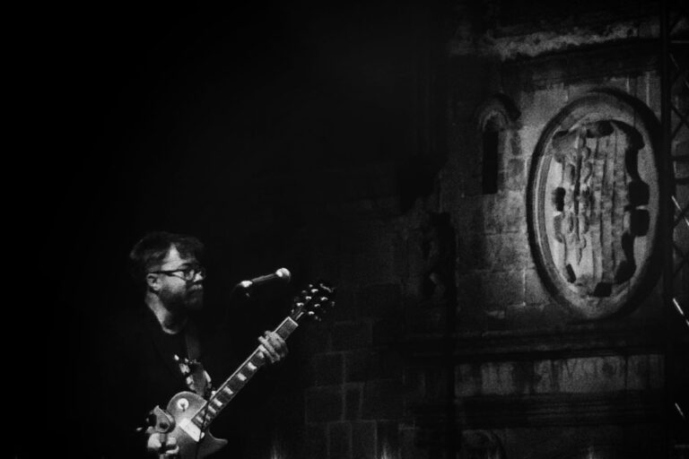 Guitarist in the Old Town of Caceres in front of a medieval shield.